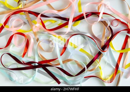 Bunte schmale Satinbänder breiten sich auf einem weißen Hintergrund chaotisch aus. Abstrakter Regenbogenhintergrund. Horizontales Foto. Stockfoto