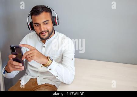 Junge hört Musik mit Kopfhörern. Mann mit Handy. Mann im Café, der auf das Handy schaut. Lifestyle. Arbeitspause. Stockfoto