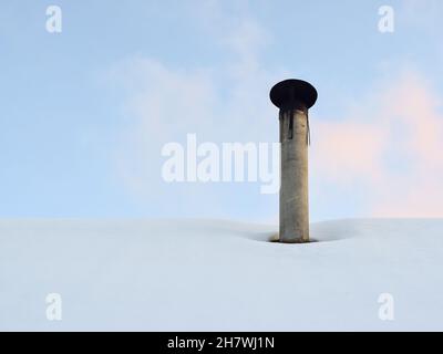 Ein Ofenrohr auf einem schneebedeckten Dach. Heizperiode im privaten Sektor. Horizontales Foto. Stockfoto