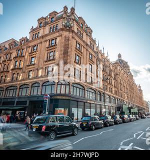 Harrods, London. Vor dem berühmten Kaufhaus im wohlhabenden Einkaufsviertel von Kensington warten Einkäufer und schwarze Taxis. Stockfoto