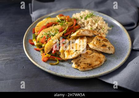 Gebratene Hühnerscheiben mit Gemüse aus rotem Paprika, Birne und Lauch, serviert mit braunem Reis auf einem blauen Teller, dunkler rustikaler Holztisch, Kopierplatz Stockfoto