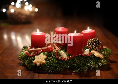 Dritter Advent - geschmückter Adventskranz aus Tannenzweigen mit roten brennenden Kerzen auf einem Holztisch in der Zeit vor Weihnachten, festliches Bokeh im Stockfoto