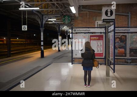 Doncaster, Großbritannien, 22nd. Mai 2021: Frau trägt nachts einen Wintermantel, während sie Informationen auf einem sauberen Bahnsteig am bahnhof von doncaster liest Stockfoto