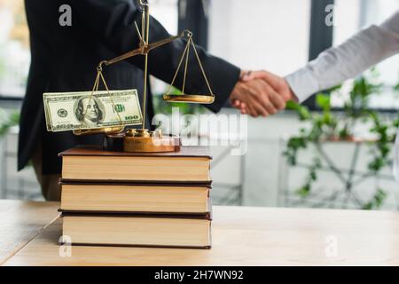 KIEW, UKRAINE - 22. SEPTEMBER 2021: Justiz wackelt mit Dollar auf Büchern in der Nähe von ausgeschnittenen Geschäftsleuten, die sich die Hände schütteln, Antikorruptionskonzept Stockfoto