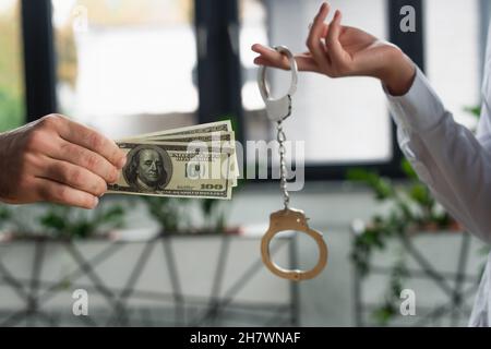 KIEW, UKRAINE - 22. SEPTEMBER 2021: Beschnittene Ansicht einer Frau, die Handschellen in der Nähe eines Mannes mit Dollar-Banknoten hält, Antikorruptionskonzept Stockfoto