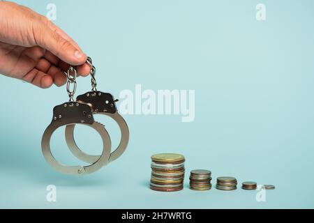 Teilansicht eines Mannes, der Handschellen in der Nähe von Stapel von Silber- und Goldmünzen auf blauem Antikorruptionskonzept hält Stockfoto