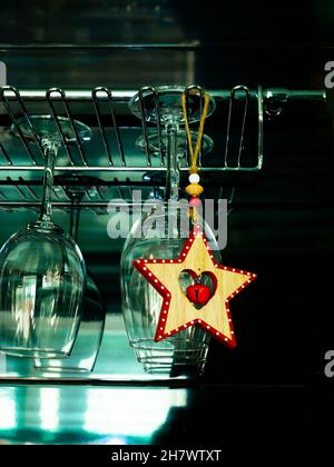 Ein Holzstern mit einer Glocke hängt an einem Weinglasaufhänger. Warten auf Weihnachten. Stockfoto