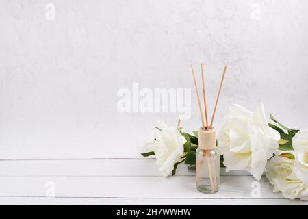 Aromatischer Reed-Freshener, Duftdiffuser-Flasche mit Duftstäbchen mit Rosenblüte auf weißem Wandhintergrund Stockfoto