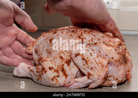 Männliche Hände bedecken rohes ganzes Huhn mit Sauce zum Kochen, Nahaufnahme. Kochen von Fleischgerichten zum Abendessen, Mittagessen. Rohes Huhn für ein Rezept Stockfoto