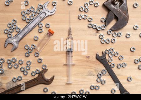 Spritze gefüllt mit Flüssigkeit, liegt eine Flasche Impfstoff auf dem Tisch zwischen einer Vielzahl von Schraubenschlüsseln und Metallmuttern. Konzept zur Herstellung von Impfstoffen. Stockfoto