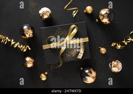 Eingewickelte Gold- und schwarze Geschenkartikel und Kugeln auf schwarzem Hintergrund mit Weihnachtsdekorationen. Blick von oben. Stockfoto