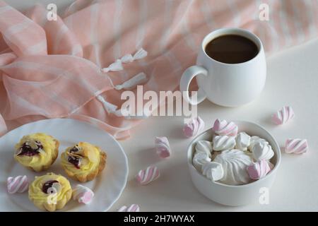 Weiße Porzellanschale aus schwarzem, stark heißem Kaffee, Tee auf hellem Hintergrund mit zarten Marschmalchen und Kuchen, hausgemachten Kuchen. Stockfoto