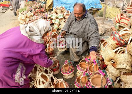 Srinagar, Indien. 24th. November 2021. Ein Kashmiri-Mann verkauft am 24. November 2021 auf einem Markt in Srinagar, Kaschmir, Indien, einen traditionellen Feuertopf Kangri. Zweige werden über einen irdenen Tontopf gewebt, um einen Kangri zu bilden. Die kangri ist mit brennender Kohle gefüllt, um die Menschen den ganzen Winter über warm zu halten. (Foto von Kamran Raashid Bhat/INA Photo Agency/Sipa USA) Quelle: SIPA USA/Alamy Live News Stockfoto