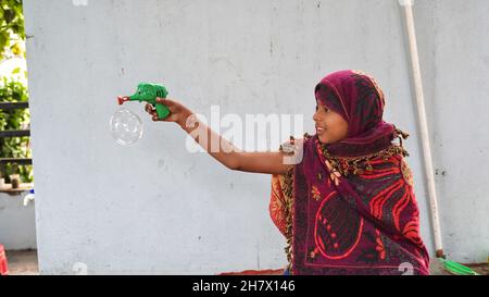 Indisches kleines Mädchen im Hinterhof spielt mit einer Bubble-Waffe. Nettes Mädchen im Sommer spielen mit Wasser und Seifenblasen close-up und kopieren Raum. Stockfoto