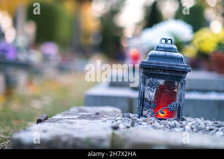 Rote Kerze brennt in einer schönen Laterne, die auf dem Grab von Allerheiligen liegt Stockfoto