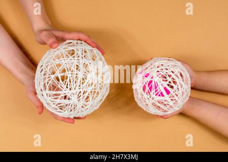 Schneemann aus Fäden. Die Hände von Kindern und Erwachsenen halten die Fäden fest. Eine Reihe von Gegenständen für die Herstellung eines handgefertigten Schneemanns. Fäden, Kugeln, Kleber. Schritt 4. Stockfoto