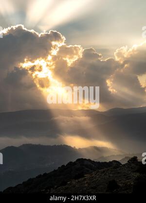 Helle Sonnenstrahlen leuchten bei Sonnenuntergang durch dunkle Wolken über dem Berg. Dramatischer Himmel im Winter Stockfoto