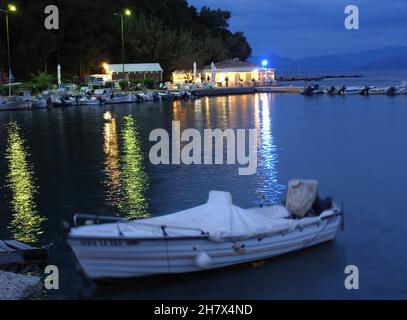 Abend in Kanoni, ein kleines Boot im Hafen mit Blick auf Flisvos Cafe und Taverna, Mouse Island, Pontikonissi, Korfu, Griechenland Stockfoto