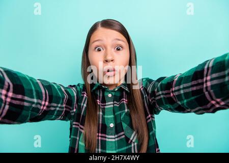 Foto von beeindruckt funky Schulmädchen gekleidet karierte Kleidung große Augen tacking Selfie isoliert teal Farbe Hintergrund Stockfoto