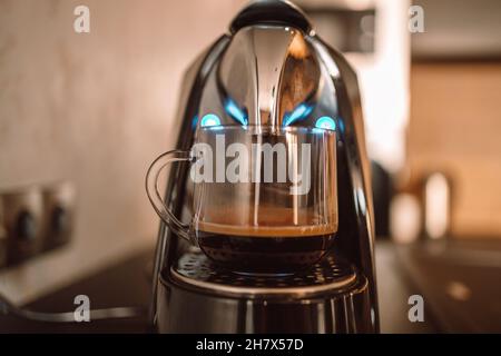 Frisch gebrühter Kaffee wird aus der professionellen Espressomaschine in eine Glastasse in der Küche zu Hause gegossen Stockfoto