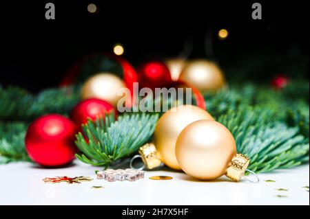 Dekoration für Weihnachtsferien. Goldene und rot schimmernde Weihnachtskugeln, Tannengrün, Konfetti-Sterne und Weihnachtslichter auf weißem Hintergrund. Stockfoto