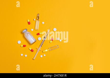 Impfstoff und Spritze, verschiedene pharmazeutische Medikamente Pillen, Tabletten und Kapseln gelber Hintergrund. Gesundheitswesen und medizinisches Konzept. Stockfoto