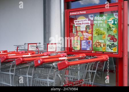 Goppingen, Deutschland - 23. Mai 2021: Rotes Werbeschild und Einkaufswagen für Lebensmittel vor einem Penny-Supermarkt in deutschland. Schräge Ansicht von beh Stockfoto