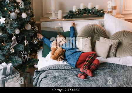 Ein charmantes Mädchen wachte mit ihrem Teddybär unter dem Weihnachtsbaum auf Stockfoto