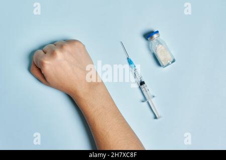 Hand des Antivaxxers in der Nähe der Spritze mit Covid-19-Impfstoff. Eine Person, die eine Immunisierung gegen Coronavirus verweigert. Covid Skepsis Konzept Stockfoto