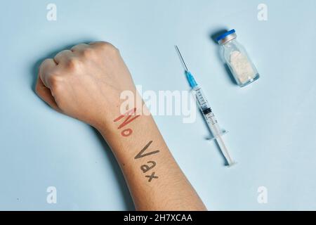 Hand des Antivaxxers in der Nähe der Spritze mit Covid-19-Impfstoff. Eine Person, die eine Immunisierung gegen Coronavirus verweigert. Covid Skepsis Konzept Stockfoto