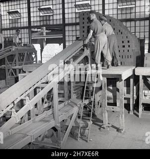 1950s, historisch, zwei männliche Arbeiter, die auf einer Holzplattform stehen und neu hergestellte Steine in der Ziegelei der London Brick Company, Stewartby, Bedford, England, stapeln. Mitte 1930s befand sich auf dem Gelände der größte Ofen der Welt, der 500 Millionen Ziegelsteine pro Jahr produzierte. Es gab 167 Schornsteine an den Werken. Stockfoto