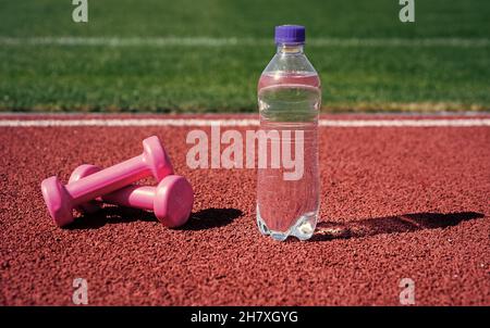 Hydratation nach Fitness. Gesunder Lebensstil. Wasserhaushalt im Körper beim Training. Langhanteln und Flasche auf Laufstrecke. Sportgerät und -Ausrüstung. Humbb Stockfoto