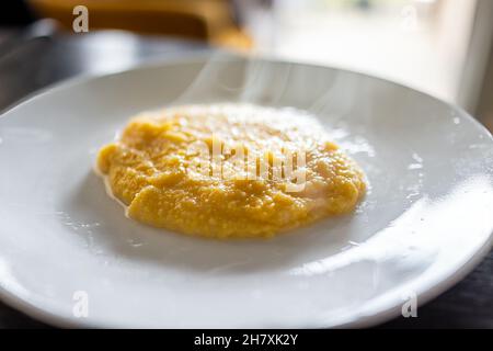 Gekochte gelbe südamerikanische Maisgrütze auf dem Teller als Frühstücksbrei mit heißem Dampf, der aufsteigt, und einer Textur aus gesundem Getreide Stockfoto