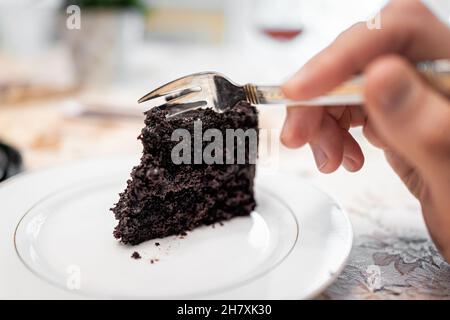 Nahaufnahme Makro der Gabel Schneiden dunkel Französisch Tod durch Schokolade geschichtete dunkle Kuchen Scheibe auf weißem Teller mit Kakao Zuckerguss Textur Stockfoto