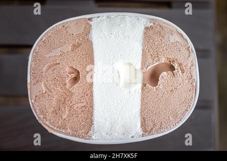 Flat top Lay Ansicht von Container Karton aus dunkler und Milch Schokolade Vanille neapolitanischen Eis gefrorenen Dessert Gelato mit Textur der Molkerei gekauft Stockfoto