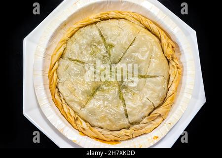 Flat Top Lay Blick nach unten Nahaufnahme von Filo Teig Spanakopita ganzen Kuchen auf weißem Teller isoliert schwarzen Hintergrund als traditionelle griechische Küche mit Witz gemacht Stockfoto