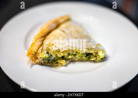 Makro-Nahaufnahme von Filoteig Spanakopita Tortenscheibe serviert auf weißem Teller isoliert schwarzen Hintergrund als traditionelle griechische Lebensmittel mit Spinat und che Stockfoto