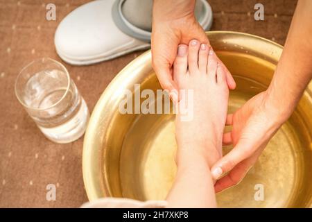 Waschen des weiblichen Fußes in einem speziellen Behälter durch männlichen Masseur im Spa-Salon Stockfoto