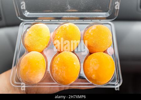 Makro-Nahaufnahme von Mann Person Hand hält Store gekauft kalt gefrorenes Eis gefüllt Mochi Reiskuchen Japanisches Dessert mit Mango oder Passionsfrucht Tropica Stockfoto