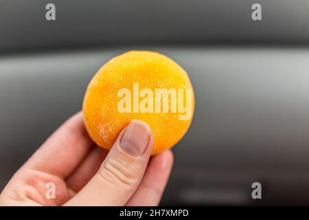 Makro Nahaufnahme einer Frau weibliche Hand hält Eis gefüllt Mochi Reis kalt süßen Kuchen Japanischen Dessert mit Mangofrucht-Geschmack und Stärke Stockfoto