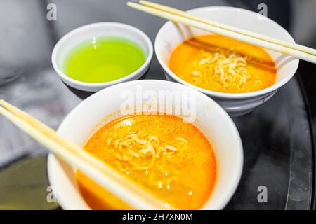 Makro-Nahaufnahme Textur von zwei würzigen roten Ramen Nudelsuppe weißen Schalen mit Essstäbchen japanischen asiatischen Mahlzeit und grünem Tee Tasse Stockfoto
