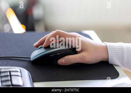 Eine Hand, die eine optische Computermaus hält, um auf dem Bildschirm zu navigieren. Das Peripheriegerät wird auf einem Mousepad bewegt, um durch das Gerät zu blättern oder zu blättern Stockfoto