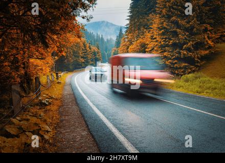 Verschwommene Autos auf der Straße im Herbst Nebelwald an regnerischen Tagen Stockfoto