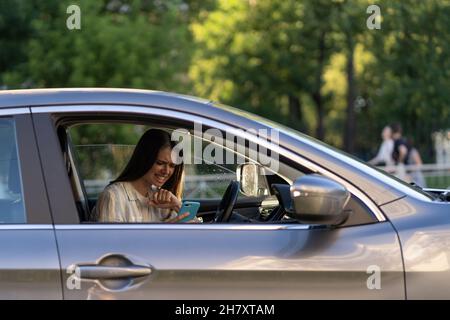 Weinendes junges Mädchen las Nachricht auf dem Handy. Frustriert verärgert junge Frau am Fahrersitz im Auto Stockfoto