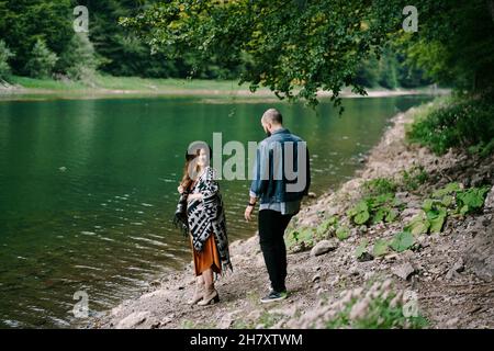 Der Mann geht hinunter zu einer Schwangeren am Ufer eines Sees im Wald Stockfoto