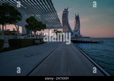 Lusail Corniche am Yachthafen in Lusail City, Katar, Sonnenuntergangsaufnahme, die Menschen zeigt, die auf der Promenade mit Skyline im Hintergrund spazieren und sitzen Stockfoto