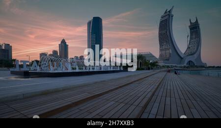 Lusail Corniche am Yachthafen in Lusail City, Katar, Sonnenuntergangsaufnahme, die Menschen zeigt, die auf der Promenade mit Skyline im Hintergrund spazieren und sitzen Stockfoto