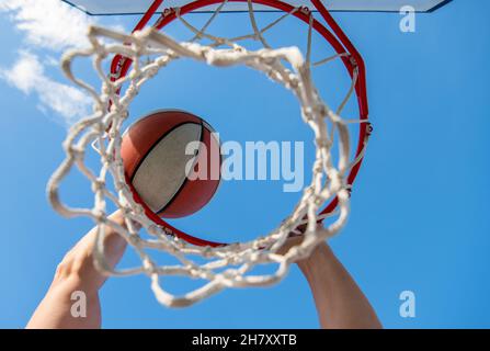 Guy dunking Basketball Ball durch Netzring mit Händen, Ziel Stockfoto