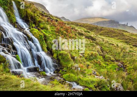 Goldenes Licht und lebhafter, farbenfroher Sonnenuntergang- oder Sonnenaufgangshimmel über der dramatischen Landschaft des Old man of Storr mit dem Wasserfall Bride's Veil Falls auf der Isle of Stockfoto