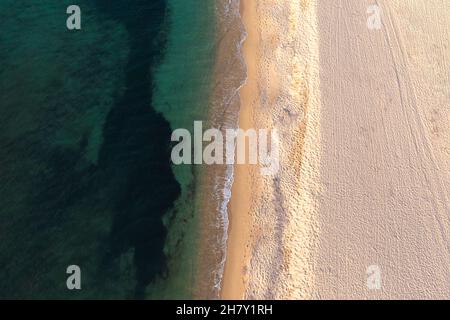 Luftaufnahme von oben auf den wunderschönen weißen Sandstrand, der von klarem türkisfarbenem Meerwasser durchflutet ist. Stockfoto